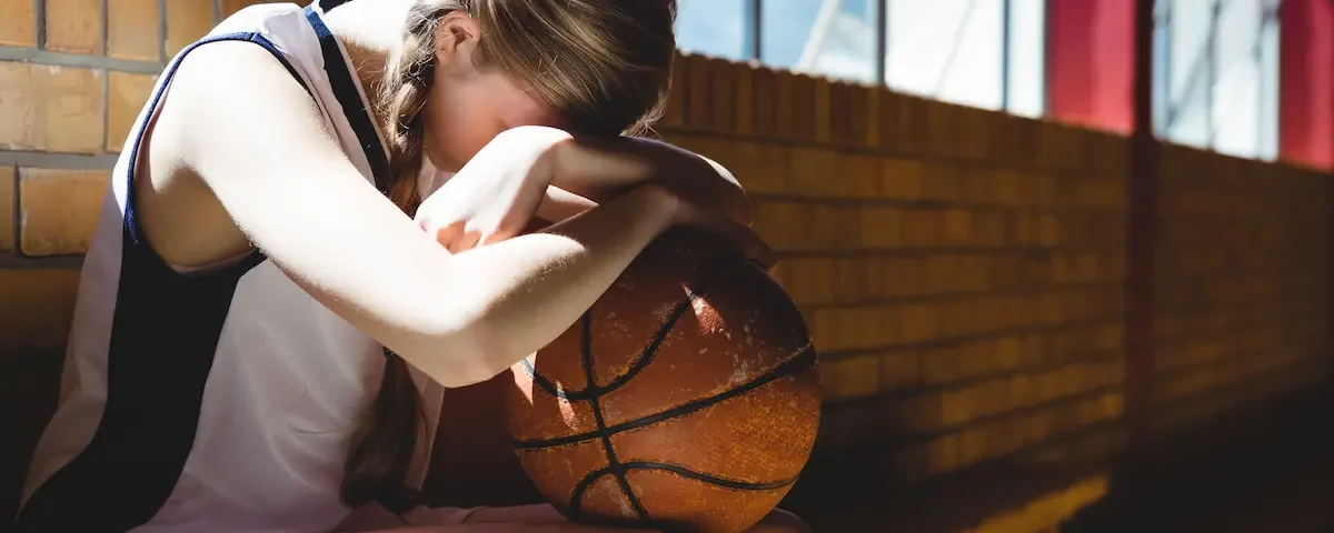 Tired, discouraged female basketball player rests head on ball after athletic bullying