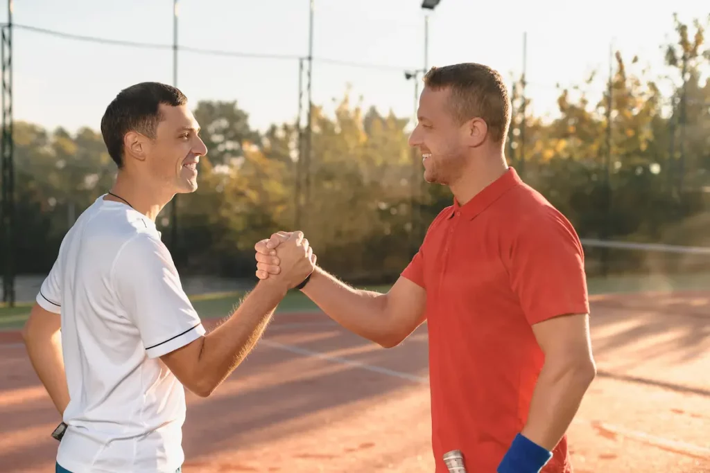 Two males embrace on the tennis court to build strong athletic program relationships