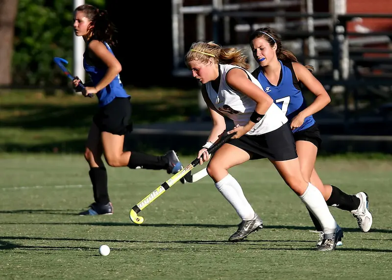 Three lacrosse athletes running down a lacrosse field. 