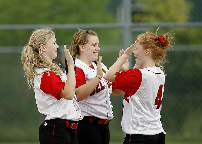 Three softball players who play for fun high-five during a softball game.