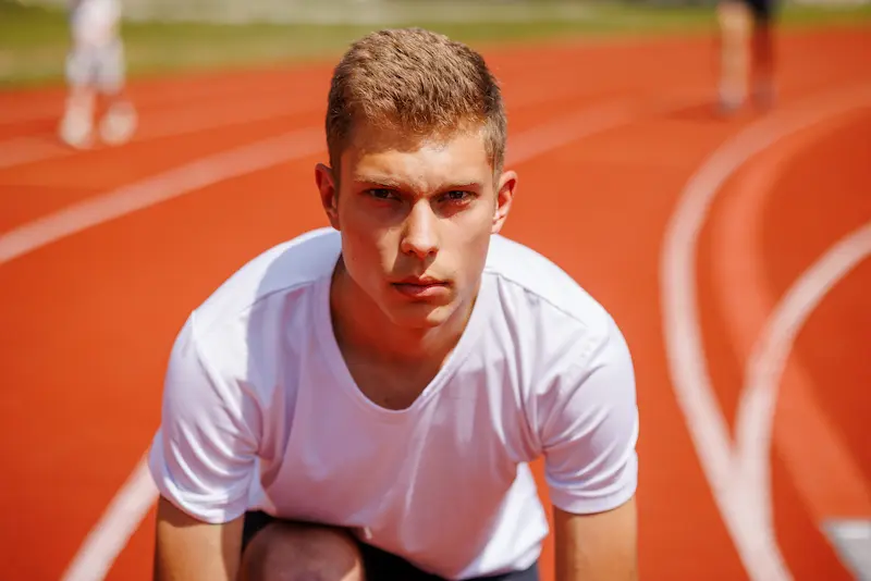 A young male athlete is poised for a track race. 