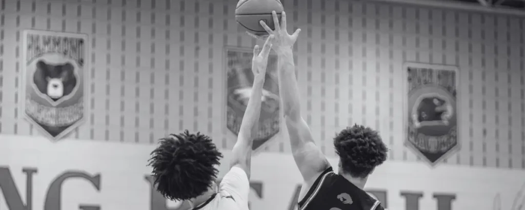 Two opposing basketball players compete to get to the ball. 