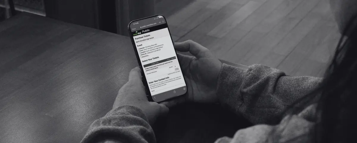 Fan holds a smartphone showing an Eventlink ticket purchase page for a school event.
